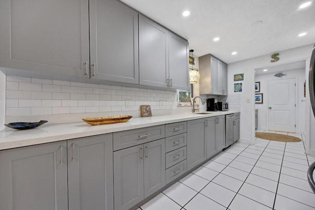 kitchen with light tile patterned flooring, sink, stainless steel dishwasher, gray cabinets, and backsplash