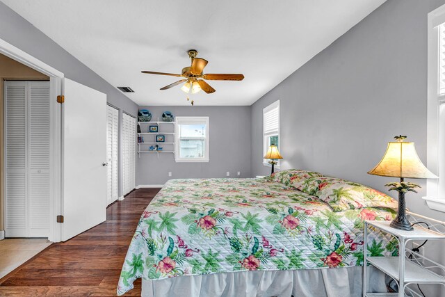 bedroom featuring multiple closets, dark wood-type flooring, and ceiling fan