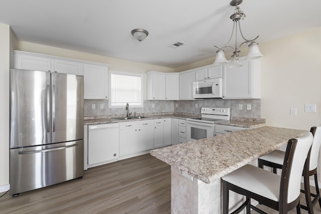 kitchen featuring a breakfast bar, pendant lighting, white cabinetry, sink, and white appliances