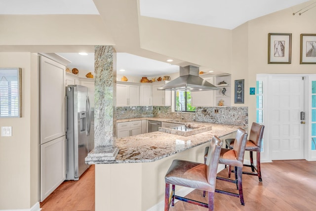 kitchen with appliances with stainless steel finishes, a kitchen breakfast bar, light stone counters, island range hood, and kitchen peninsula