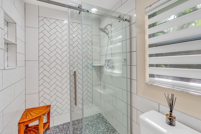 bathroom with a shower with door, tile walls, and toilet