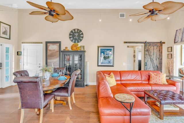 living room featuring light hardwood / wood-style flooring, ceiling fan, a towering ceiling, ornamental molding, and a barn door