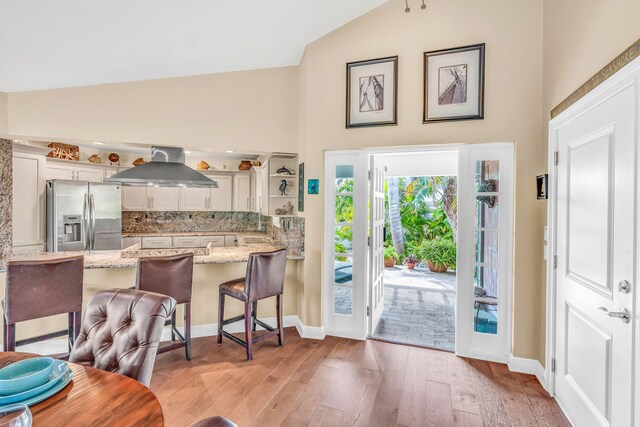 kitchen featuring a breakfast bar area, stainless steel refrigerator with ice dispenser, light stone counters, island range hood, and kitchen peninsula