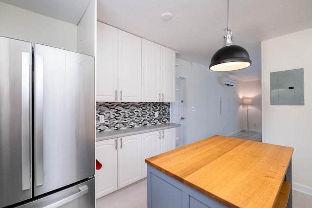 kitchen featuring stainless steel refrigerator, white cabinets, decorative backsplash, hanging light fixtures, and electric panel