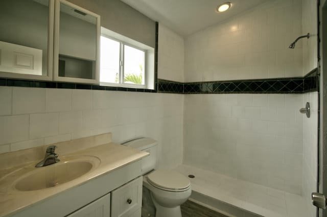 bathroom with tiled shower, lofted ceiling, toilet, and vanity