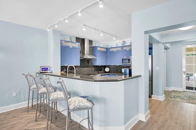 97501 Overseas Hwy Unit 113, Key Largo, FL 33037 - kitchen featuring wall chimney exhaust hood, appliances with stainless steel finishes, a kitchen breakfast bar, decorative backsplash, and baseboards