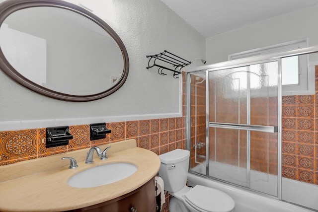 full bathroom featuring bath / shower combo with glass door, toilet, a wainscoted wall, vanity, and tile walls