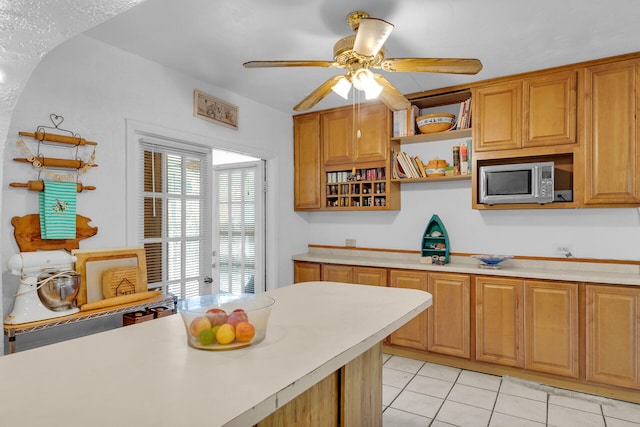 kitchen with light tile patterned floors, light countertops, stainless steel microwave, and open shelves