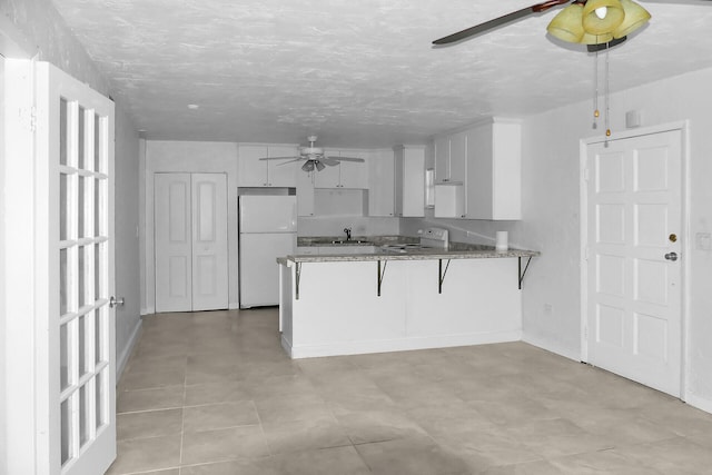 kitchen with a peninsula, stove, a sink, a ceiling fan, and freestanding refrigerator