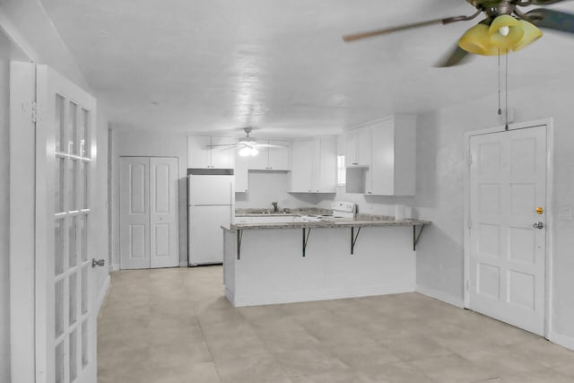 kitchen featuring white appliances, white cabinets, a ceiling fan, a peninsula, and a kitchen bar