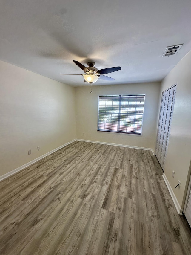 empty room with ceiling fan, wood finished floors, visible vents, and baseboards