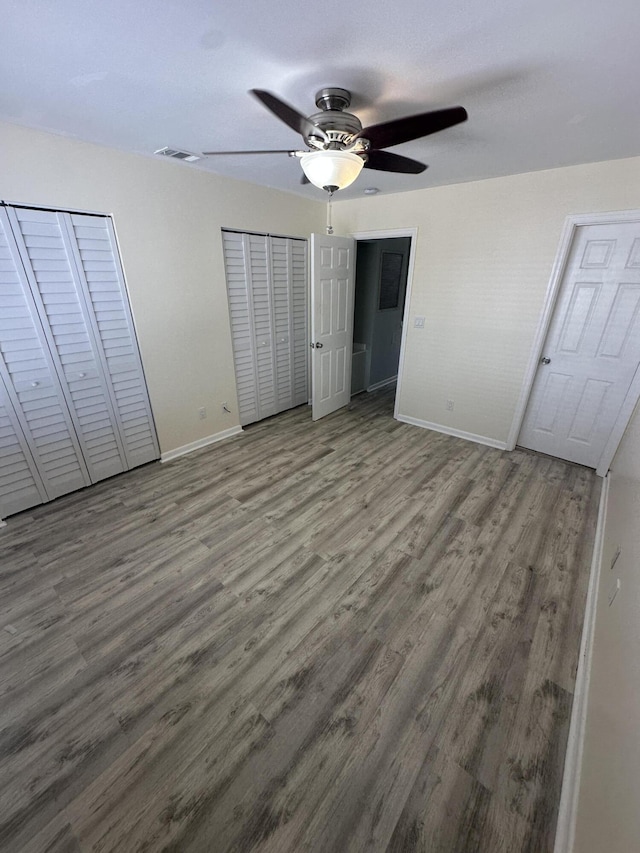 unfurnished bedroom featuring visible vents, two closets, baseboards, and wood finished floors