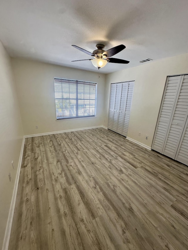 unfurnished bedroom featuring baseboards, visible vents, a textured ceiling, light wood-type flooring, and two closets