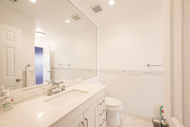 bathroom featuring visible vents, wainscoting, toilet, vanity, and tile walls