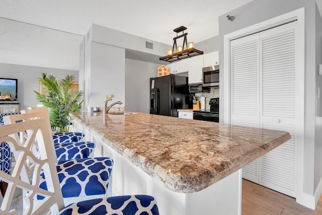 kitchen featuring decorative light fixtures, a breakfast bar area, white cabinets, black appliances, and light hardwood / wood-style flooring