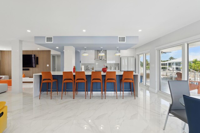 kitchen with a breakfast bar, white cabinetry, a spacious island, hanging light fixtures, and wall chimney exhaust hood