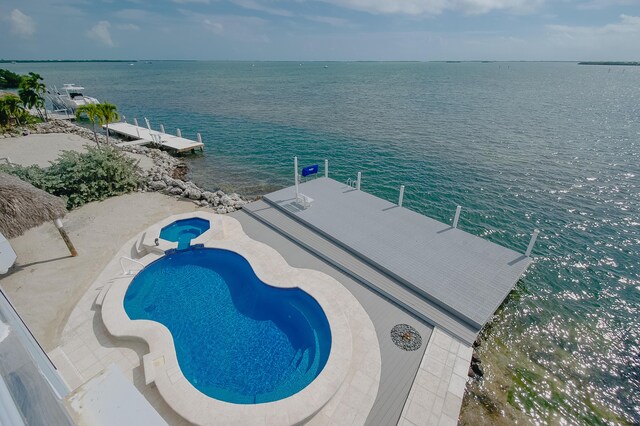 view of swimming pool with a dock, a patio, and a water view