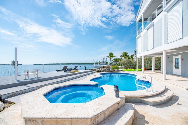 view of pool featuring an in ground hot tub, a water view, and a patio