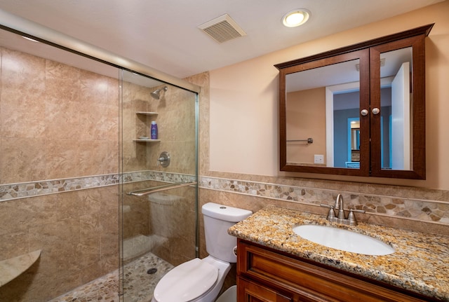 bathroom featuring walk in shower, vanity, toilet, and tile walls