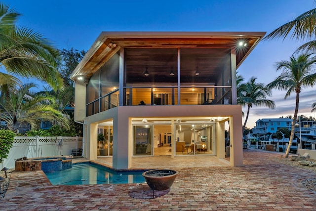 back house at dusk with a swimming pool with hot tub, a patio, and a balcony