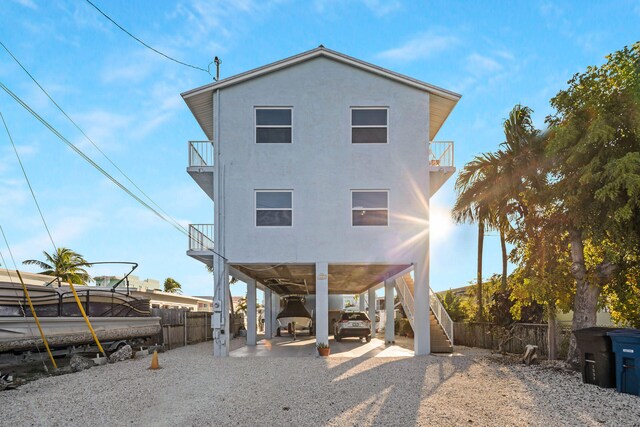 rear view of property featuring a balcony, fence, stairs, stucco siding, and a carport