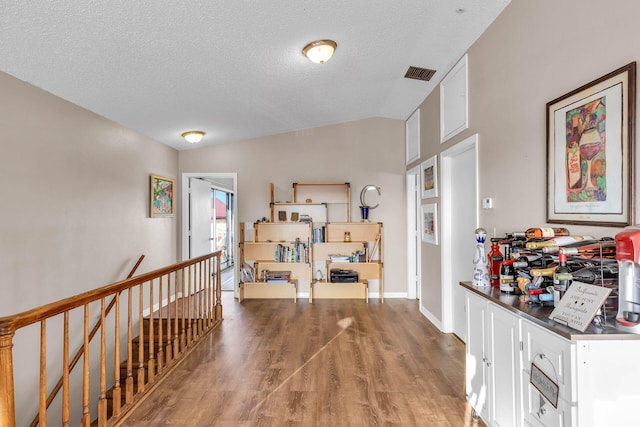 hall featuring visible vents, vaulted ceiling, a textured ceiling, an upstairs landing, and wood finished floors