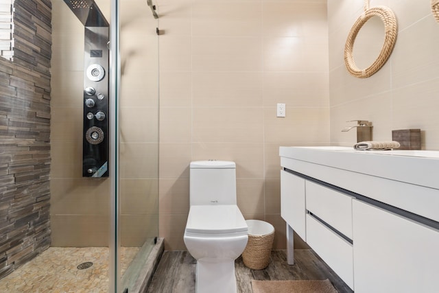 bathroom featuring vanity, a shower with door, tile walls, and toilet