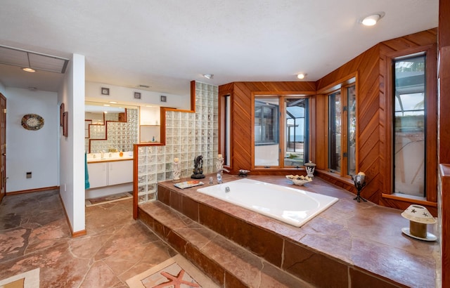 bathroom featuring a healthy amount of sunlight, wood walls, a garden tub, and vanity
