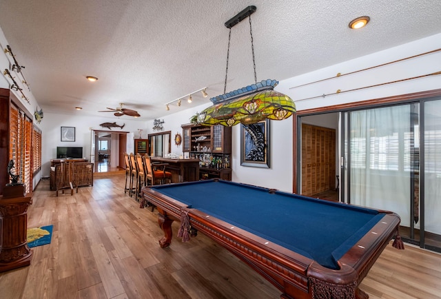 recreation room with a dry bar, light wood-style flooring, ceiling fan, and a textured ceiling