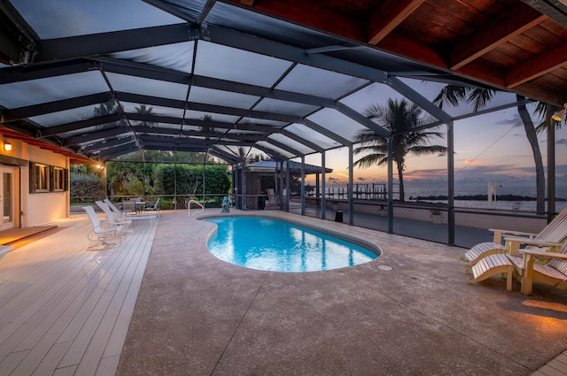 pool at dusk with a patio area, glass enclosure, and an outdoor pool