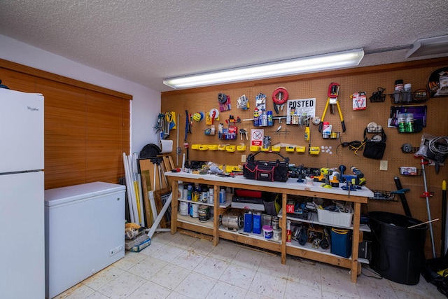 interior space featuring a workshop area, freestanding refrigerator, a textured ceiling, white fridge, and tile patterned floors