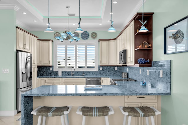 kitchen with stainless steel appliances, a tray ceiling, a kitchen breakfast bar, and hanging light fixtures