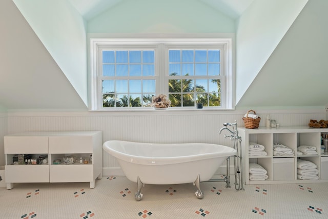 full bathroom featuring tile patterned flooring, a freestanding tub, a wainscoted wall, and vaulted ceiling