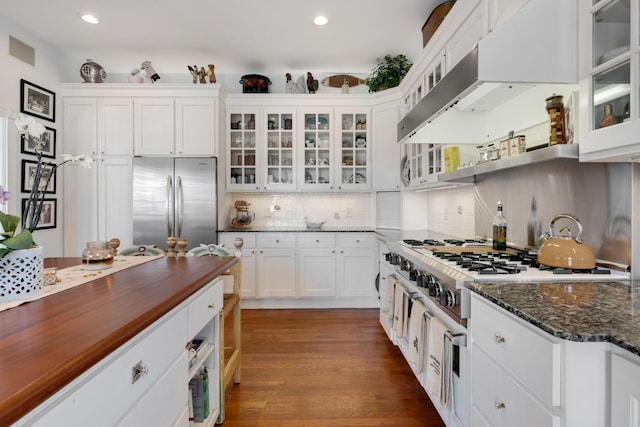 kitchen with under cabinet range hood, butcher block countertops, white cabinetry, decorative backsplash, and stainless steel fridge