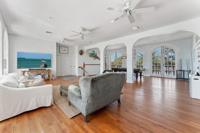 living area with arched walkways, plenty of natural light, wood finished floors, and visible vents