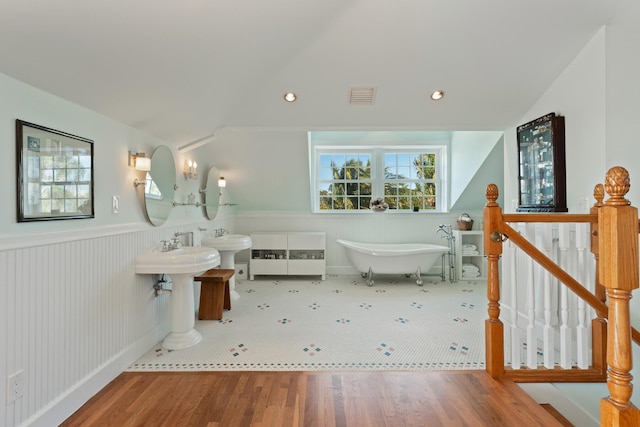 bathroom with visible vents, a wainscoted wall, wood finished floors, vaulted ceiling, and a freestanding tub