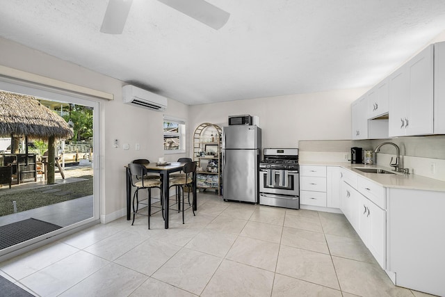 kitchen with a wall unit AC, a sink, white cabinets, light countertops, and appliances with stainless steel finishes