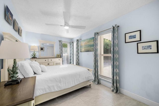 bedroom featuring ceiling fan, a textured ceiling, baseboards, and light tile patterned floors