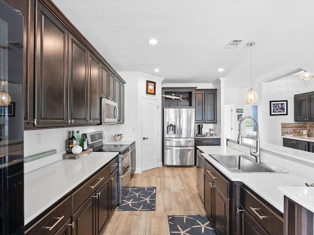 kitchen featuring appliances with stainless steel finishes, a sink, light countertops, dark brown cabinets, and hanging light fixtures