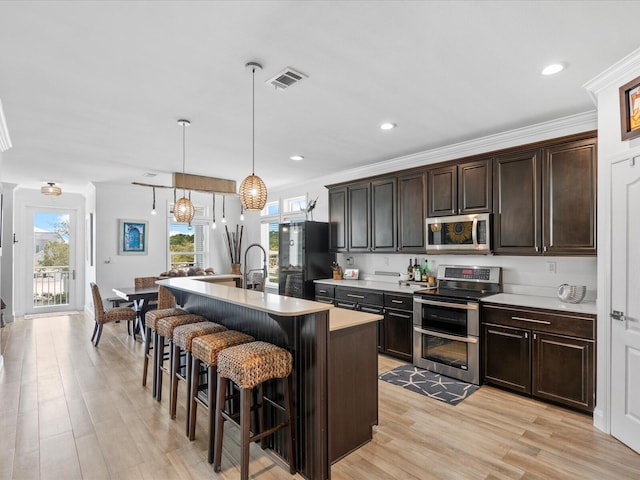 kitchen featuring appliances with stainless steel finishes, a breakfast bar area, light countertops, dark brown cabinetry, and healthy amount of natural light