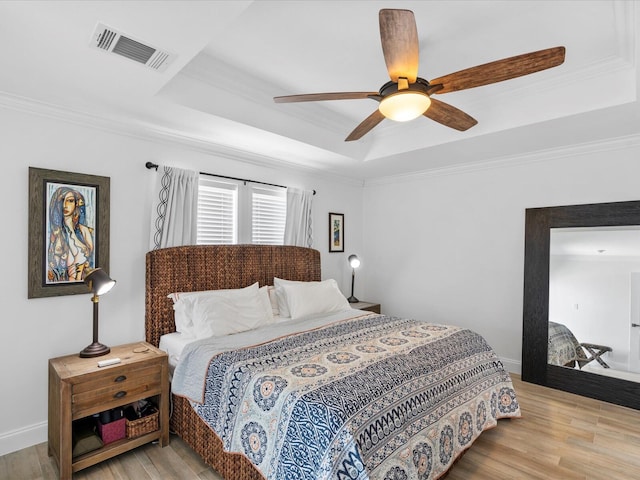 bedroom with a tray ceiling, light wood-style flooring, crown molding, a ceiling fan, and baseboards