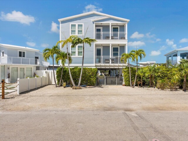 view of front of property with a balcony, dirt driveway, fence, and a carport