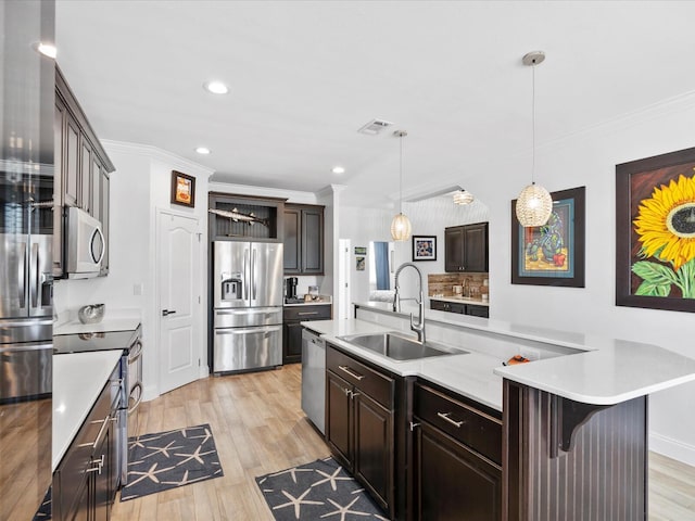 kitchen featuring stainless steel appliances, a sink, ornamental molding, light countertops, and light wood-style floors