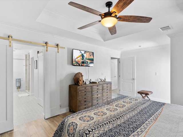 bedroom with a barn door, light wood finished floors, ornamental molding, a tray ceiling, and baseboards