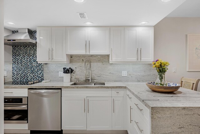 kitchen featuring sink, white cabinets, light stone counters, stainless steel appliances, and wall chimney exhaust hood