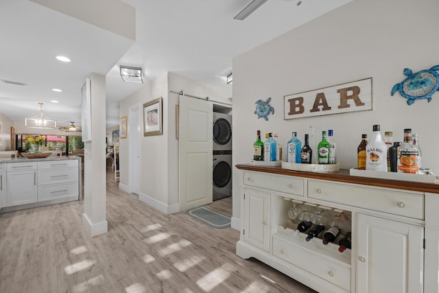 washroom featuring stacked washing maching and dryer, bar, ceiling fan, a barn door, and light hardwood / wood-style flooring