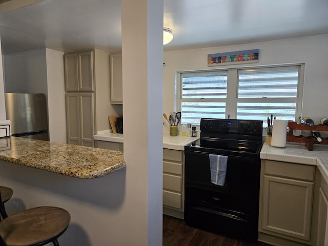 kitchen featuring dark wood-type flooring, a breakfast bar area, black electric range oven, and freestanding refrigerator