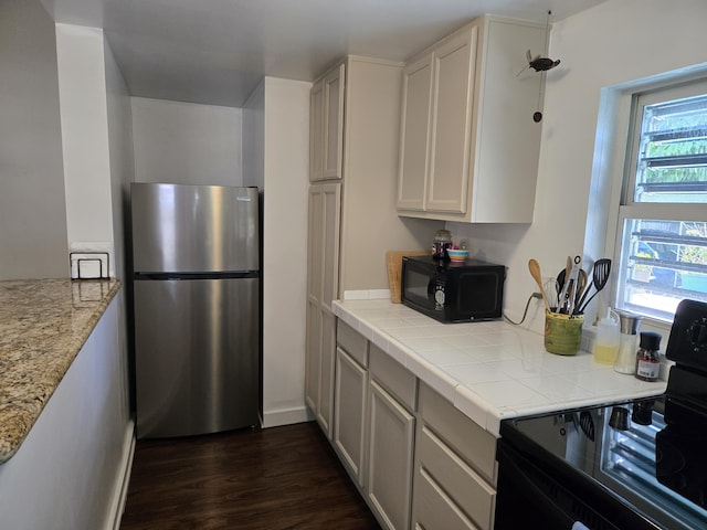 kitchen featuring dark wood-style floors, white cabinets, black appliances, and tile counters