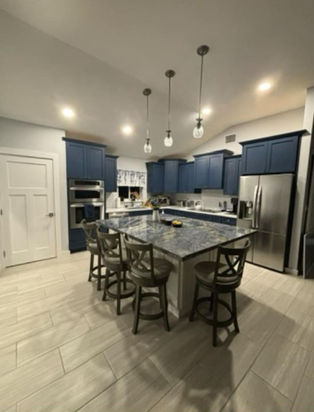 kitchen featuring blue cabinetry, a breakfast bar area, a center island, dark stone countertops, and appliances with stainless steel finishes