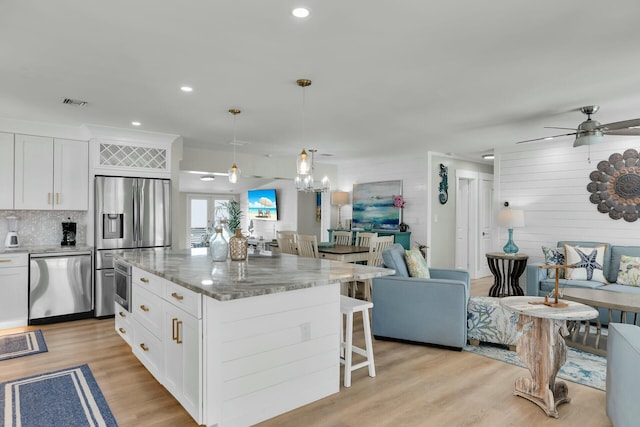 kitchen with light stone counters, open floor plan, a breakfast bar, stainless steel appliances, and white cabinets